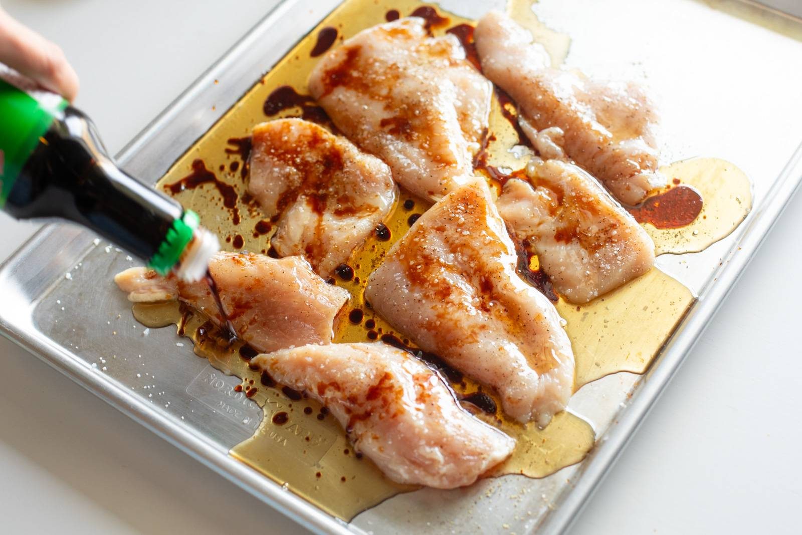 Raw chicken on a sheet pan with oil over top.