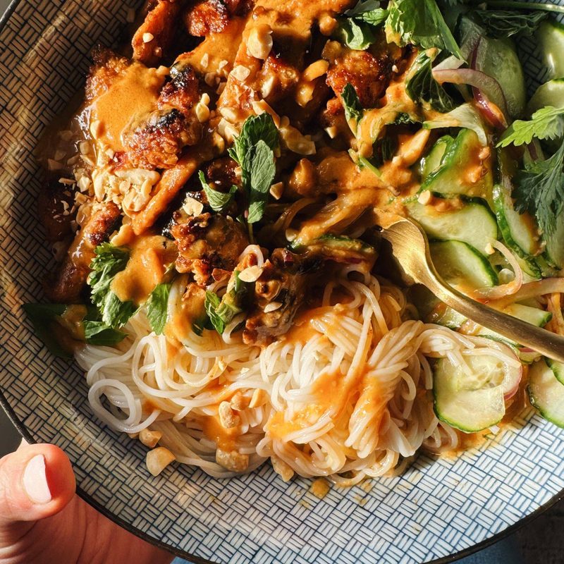 Peanut chicken in a bowl with noodles and herbs.