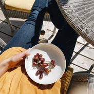 A person sitting on a chair wearing yellow top and blue jeans holding a plate having some grapes.