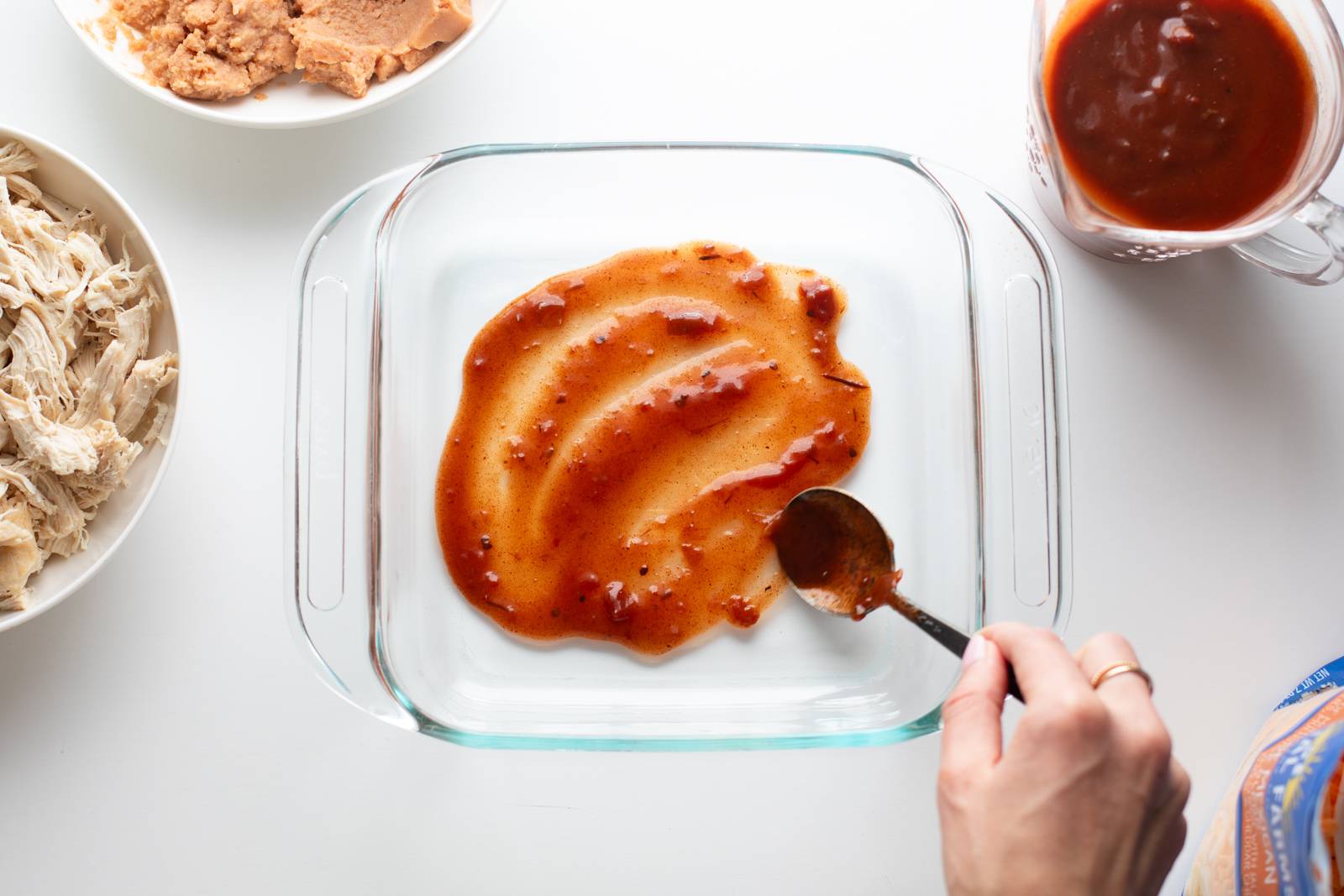 Spreading enchilada sauce in the bottom of a pan.