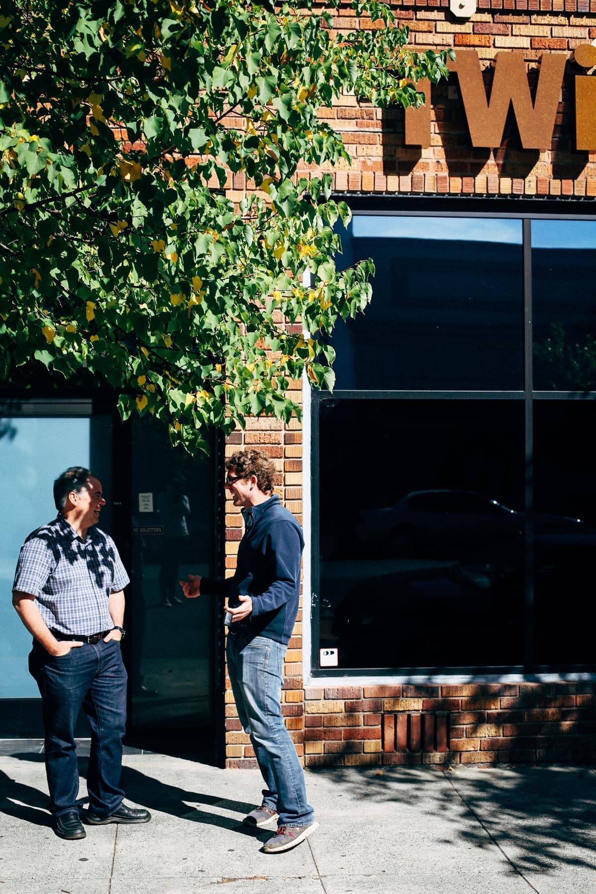 Two men talking on the sidewalk.